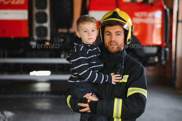 A firefighter take a little child boy to save him. Fire engine car on background.