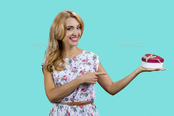 Blonde mature woman pointing at heart shape gift box. Stock Photo