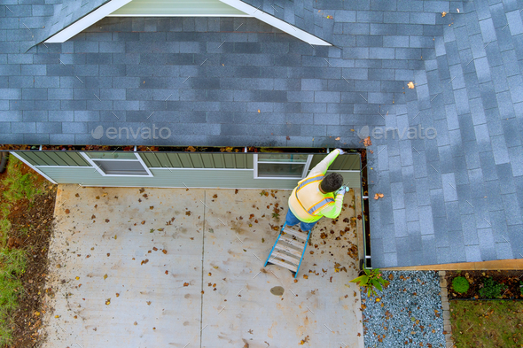 An employee is cleaning a clogged roof gutter drain with dirt, debris, fallen leaves