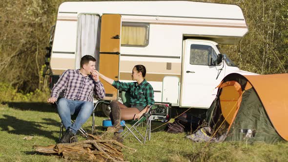 Hipster Boyfriend Kissing His Girlfriend Hand While Sitting on Camping Seats alt