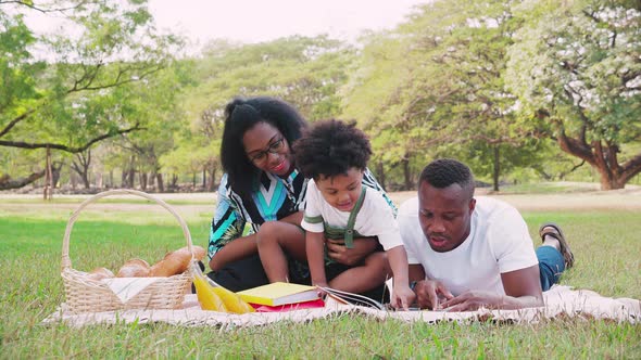 African American parent teaching a homework his son while picnic and relaxes in green park alt