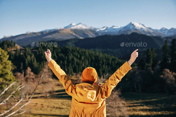 Woman standing in the fall back up her hands up in the mountains nature hike and happiness in yellow
