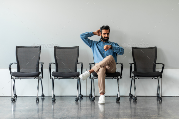 Worried indian job seeker waiting for interview far too long, sitting on chair alone in row