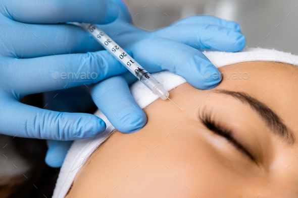 Young woman getting injection of botox or hyaluronic acid to remove wrinkles
