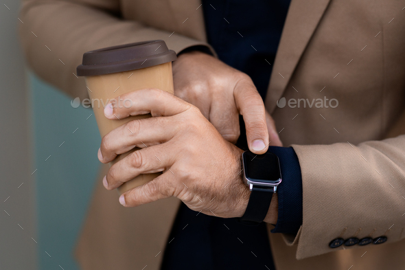 Cropped businessman checking smart watch while drinking coffee outdoors