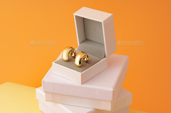 Golden earrings in jewel box on yellow background