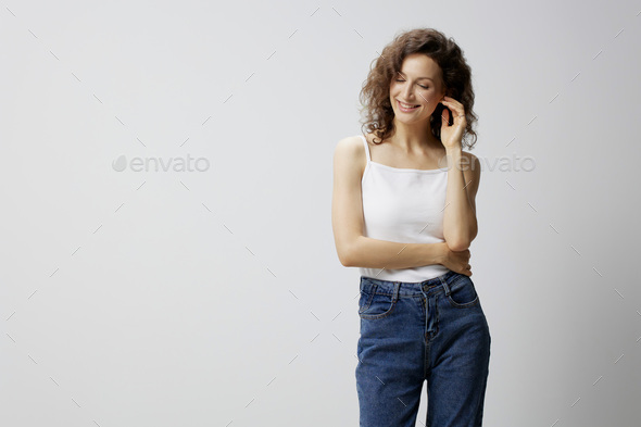 Shy cute happy curly beautiful woman in basic white t-shirt cross hands looks down aside enjoy good