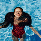 Happy woman swimming in pool in red swimsuit with loose long hair relaxed  with hands up in sunlight Stock Photo by shotprime