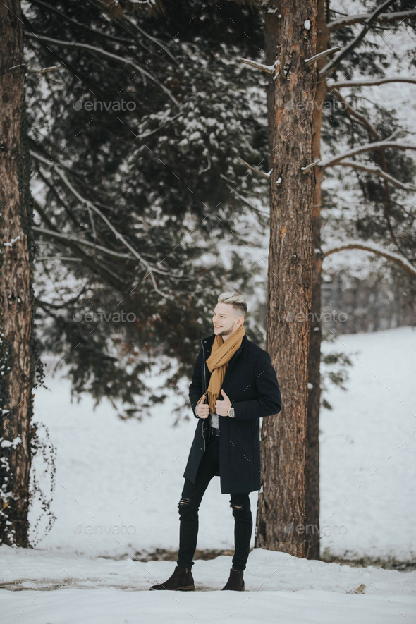 Handsome young smiling man in a black winter outfit with a brown scarf ...