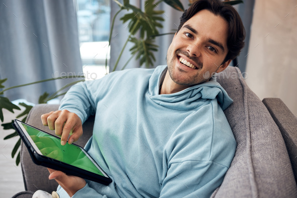 Portrait, tablet and green screen with a man gaming on a sofa in the living room of his home to rel