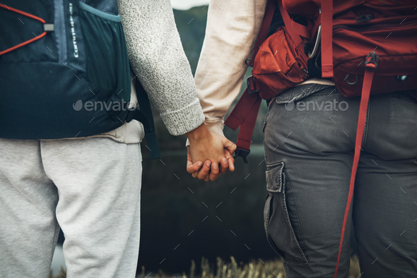 Couple, holding hands and backpack in nature for hiking, adventure or outdoor journey together. Rea