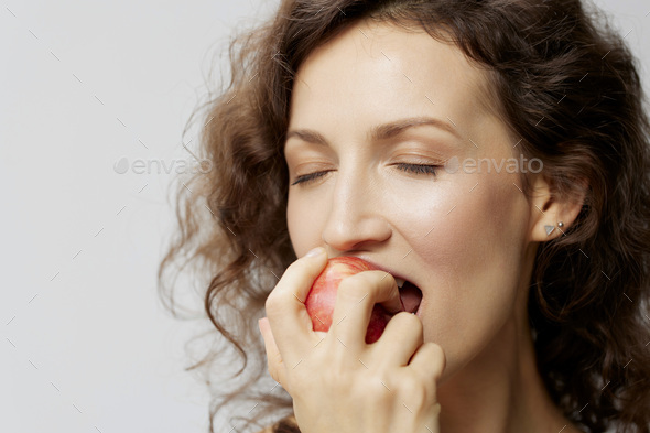 Closeup portrait of happy curly beautiful woman in basic white t-shirt enjoy fresh apple fruit