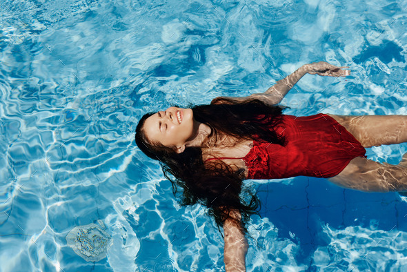 Happy woman swimming in the pool in red swimsuit with loose long hair  relaxed in the sunshine, skin Stock Photo by shotprime