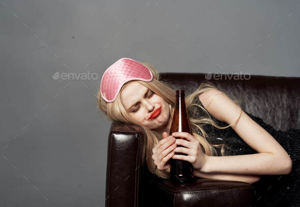 Woman with a bottle of beer and a sleep mask with closed eyes on the couch