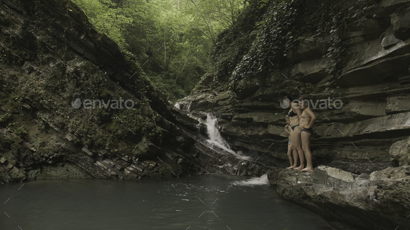 Woman with children by pond in forest. Creative. Natural waterfall with pond and bathing tourists