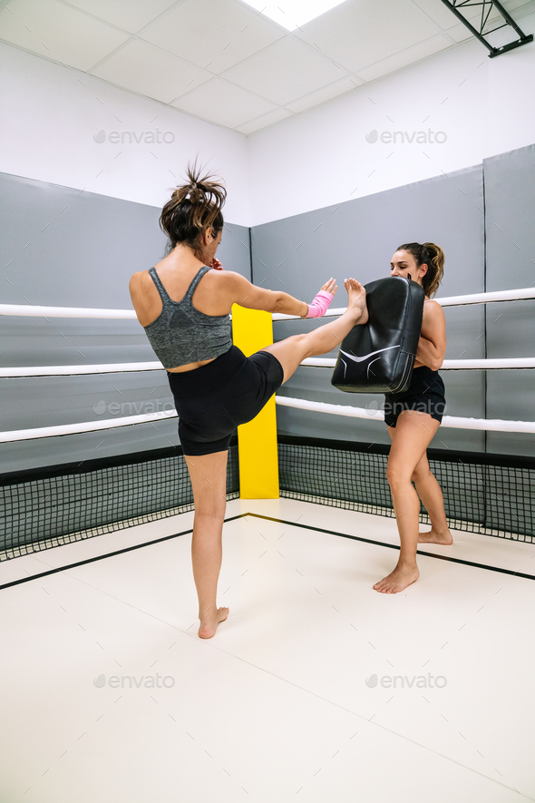Young female athlete practicing a front kick during a practice with her partner at the gym