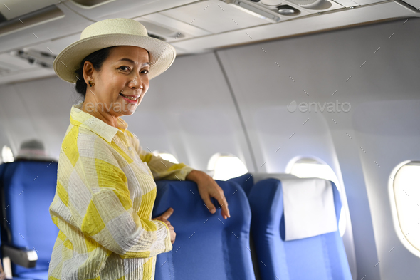 Smiling middle age female tourist with bag walking the aisle on plane ...