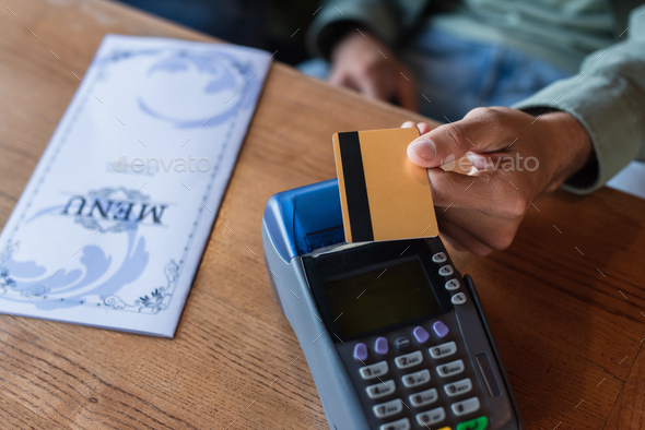 partial view of man with credit card near payment terminal and menu brochure on table