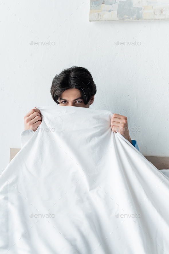 brunette man looking at camera while obscuring face with white blanket