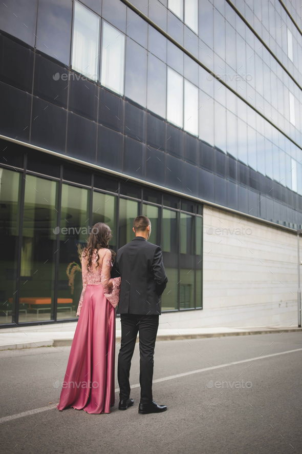 Vertical shot of a young couple standing near a modern office building with linked arms