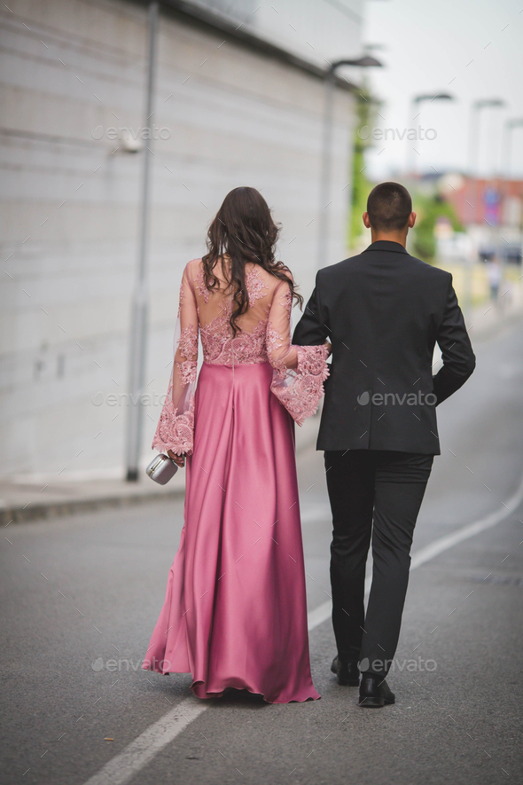 Shallow focus of a stylish elegant young couple walking through a road with linked arms