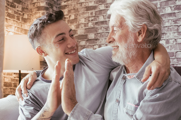 Young boy and his grandfather smile as they high five each other while sitting on the sofa at home