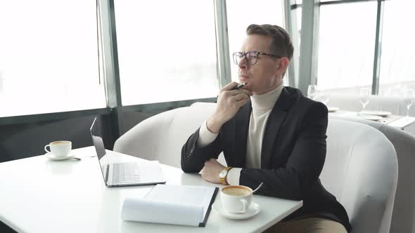 Handsome Businessman Sitting at Restaurant Table Analyzing Documentation and Contracts Taking Notes