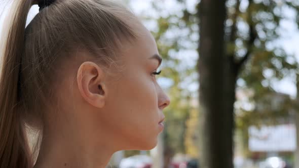 Young Pretty Female with Ponytail Looks Around Outdoors at Sunny Autumn Park