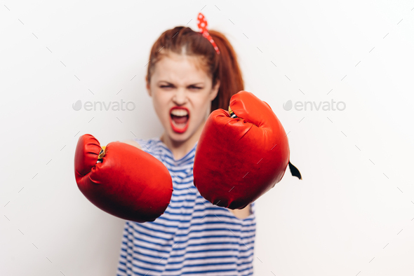 aggressive sportswoman in boxing gloves and a striped t-shirt fights on a light background