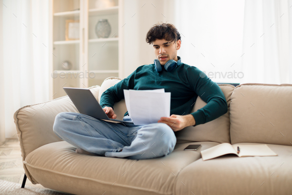 Arabic Guy Using Laptop Reading Papers On Sofa At Home
