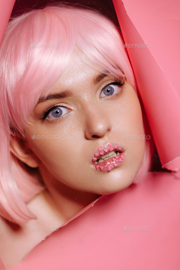 The face of a girl model with bright makeup looks into a hole in pink paper
