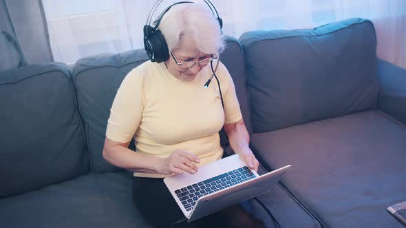 Surprised Elderly Woman with Headset Using Laptop Camera alt