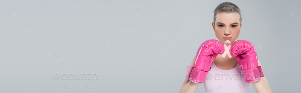 woman in pink boxing gloves looking at camera and holding breast cancer awareness ribbon isolated on