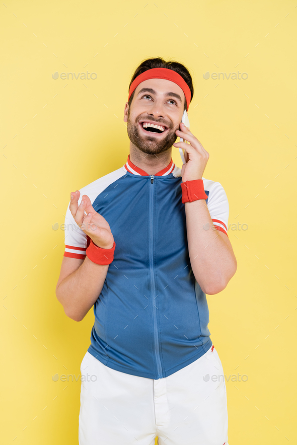 Positive sportsman talking on smartphone isolated on yellow