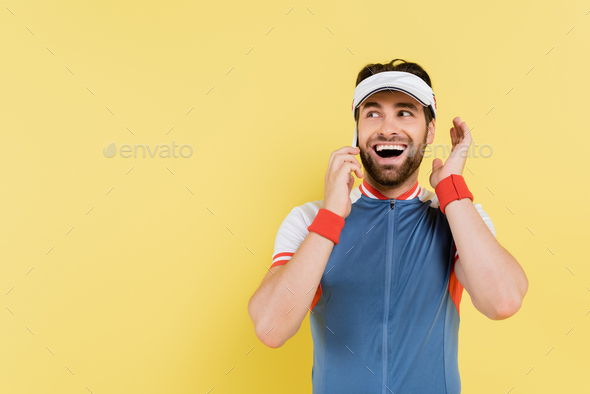 Cheerful sportsman talking on smartphone isolated on yellow