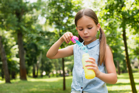girl in sleeveless blouse holding bubble blower in park