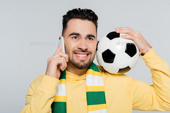 cheerful football fan in striped scarf talking on mobile phone isolated on grey