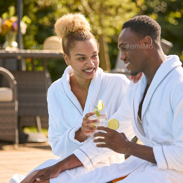 Couple Wearing Robes Outdoors Sitting Doing Cheers With Drinks By