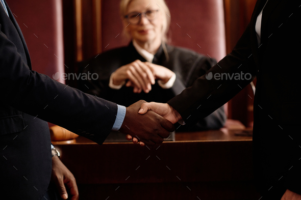 Close-up of two opposite sides of court case shaking hands against judge
