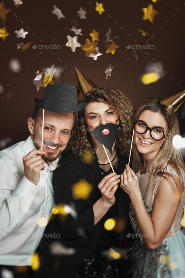 Happy people wearing party hats and using funny photo booth props are celebrating a holiday