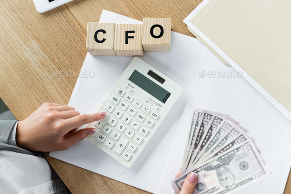 top view of chief financial officer using calculator and holding dollars near cubes with cfo