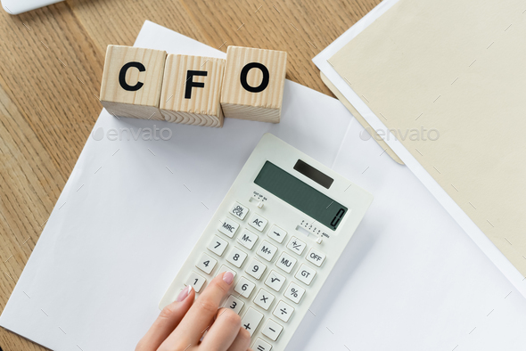 top view of chief financial officer using calculator near cubes with cfo lettering
