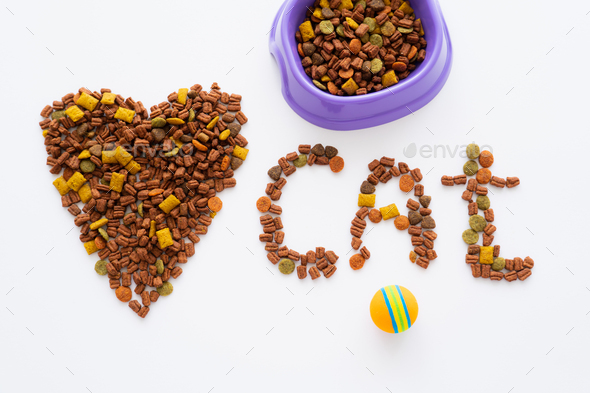 top view of heart and cat word made of dry pet food near bowl and ball isolated on white