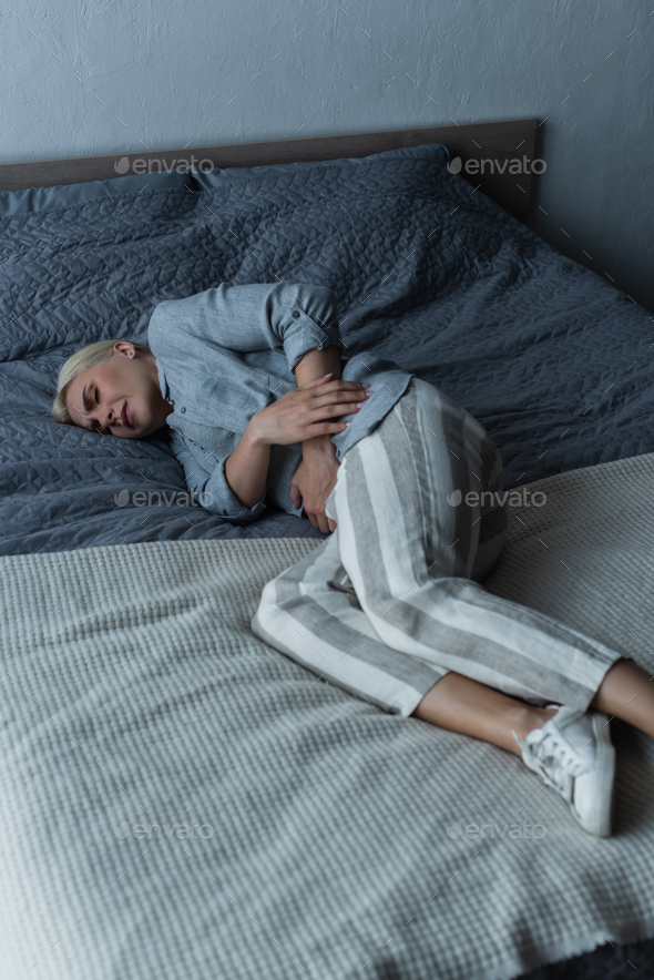 blonde woman with menopause suffering from abdominal pain and lying on