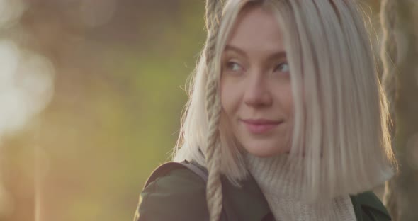 Young Woman Reads a Book on a Swing. Blonde and Beautiful Woman Smile at Sunset in an Autumn day alt