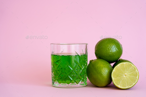 green alcohol drink in glass near fresh and organic limes on pink Stock  Photo by LightFieldStudios