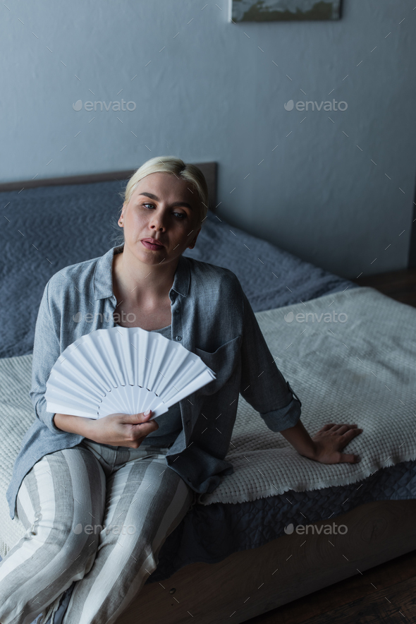 blonde woman with menopause suffering from heat and cooling with fan in