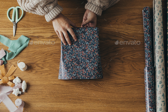 Woman in cozy sweater wrapping stylish christmas gift in festive wrapping  paper with ribbons Stock Photo by Sonyachny