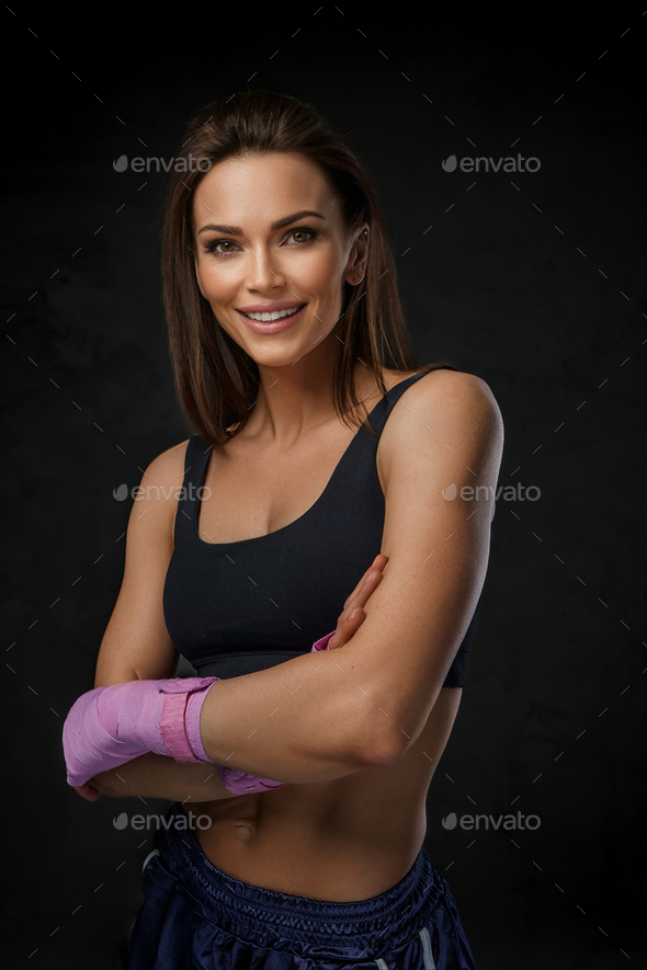Woman with a wide smile in black sports bra, posing with boxing wraps