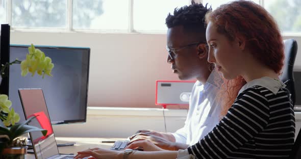 Side view of young mixed-race business team working on laptop and desktop pc in a modern office 4k alt